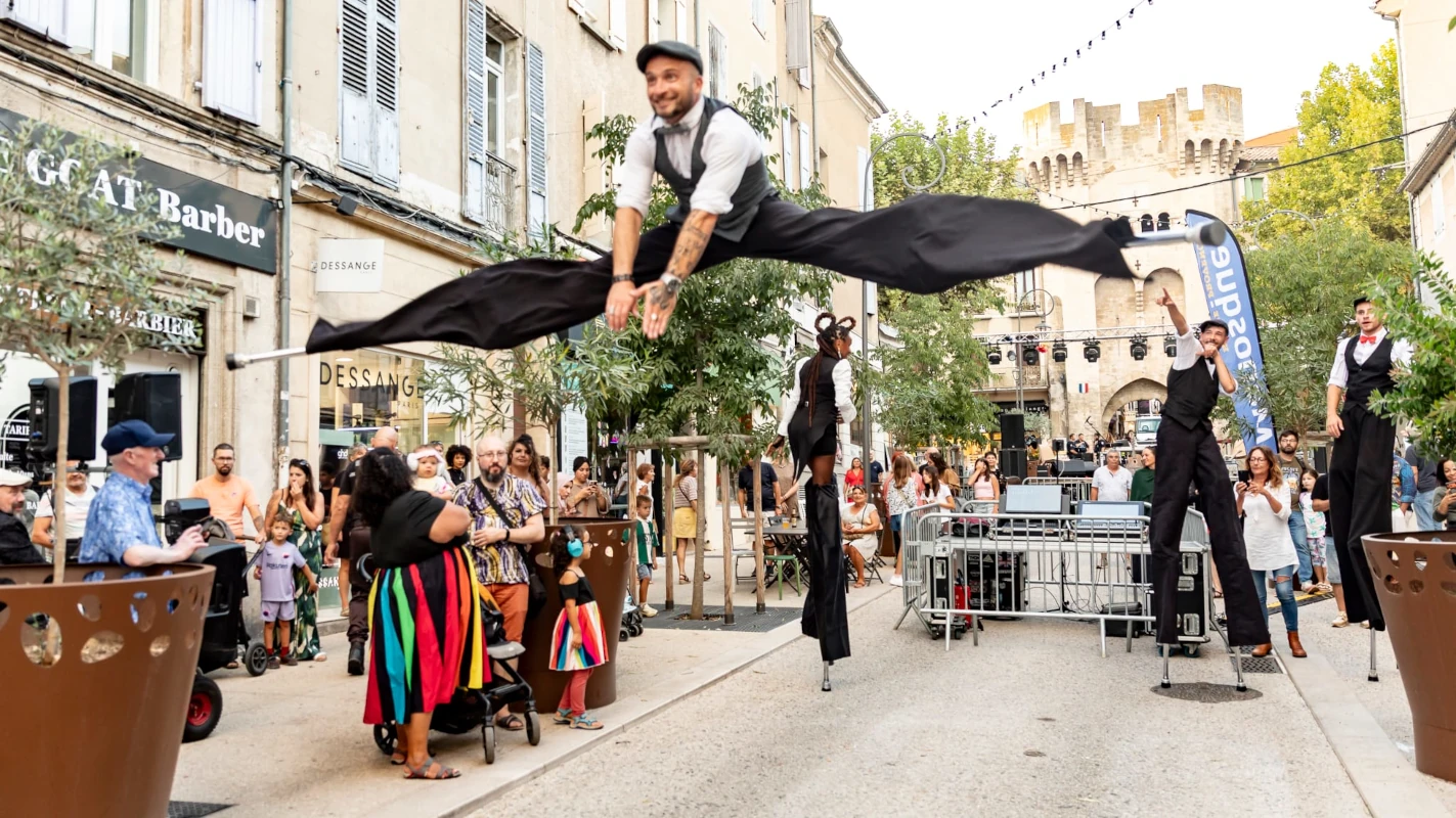 Échassiers acrobates en costumes noirs et blancs dans une rue animée, grand saut