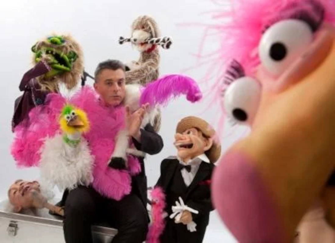 Ventriloque entouré de plusieurs marionnettes colorées