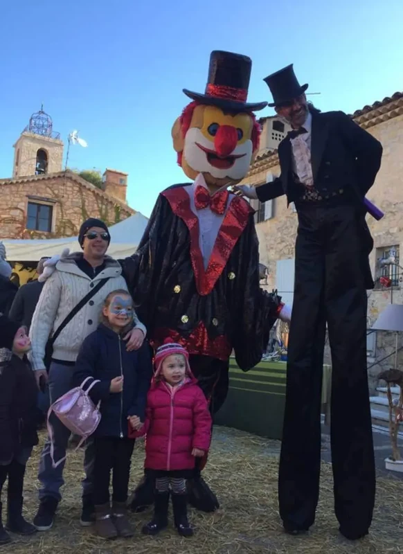 Clown géant et échassier en tuxedo avec des familles, village provençal