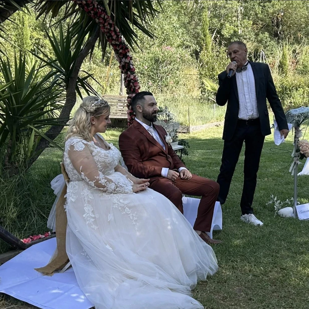 Officiant de cérémonie face aux mariés, sous une arche fleurie