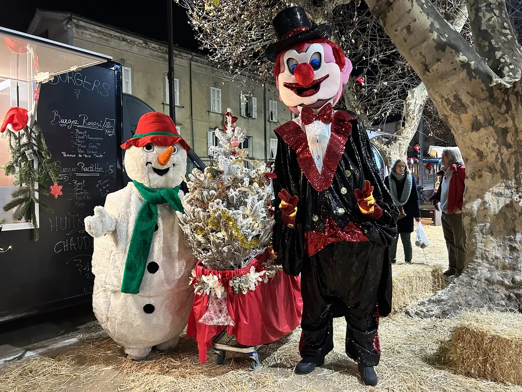 Bonhomme de neige et clown géant devant un stand de marché de Noël