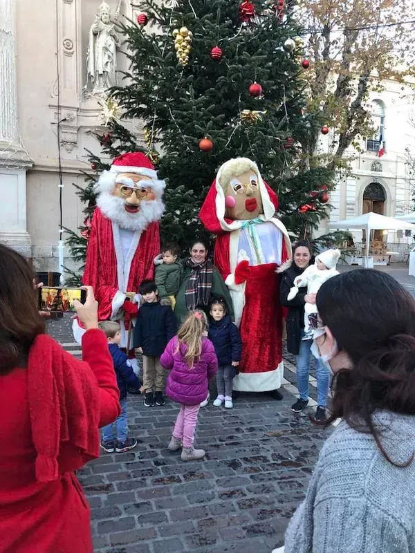 Père Noël et Mère Noël géants avec des familles devant un sapin décoré