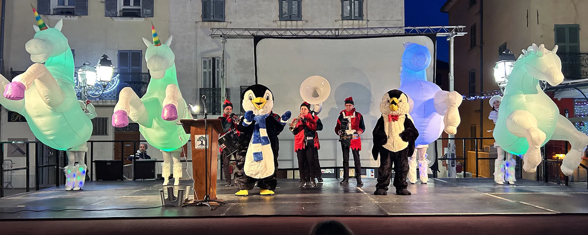 Licornes lumineuses et mascottes pingouins sur scène avec fanfare
