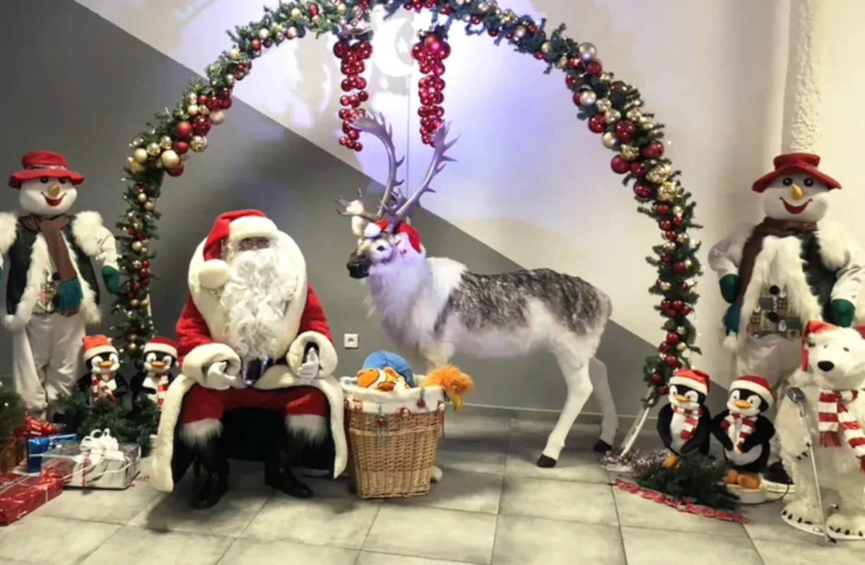 Père Noël dans un salon décoré, avec un renne et des peluches de Noël