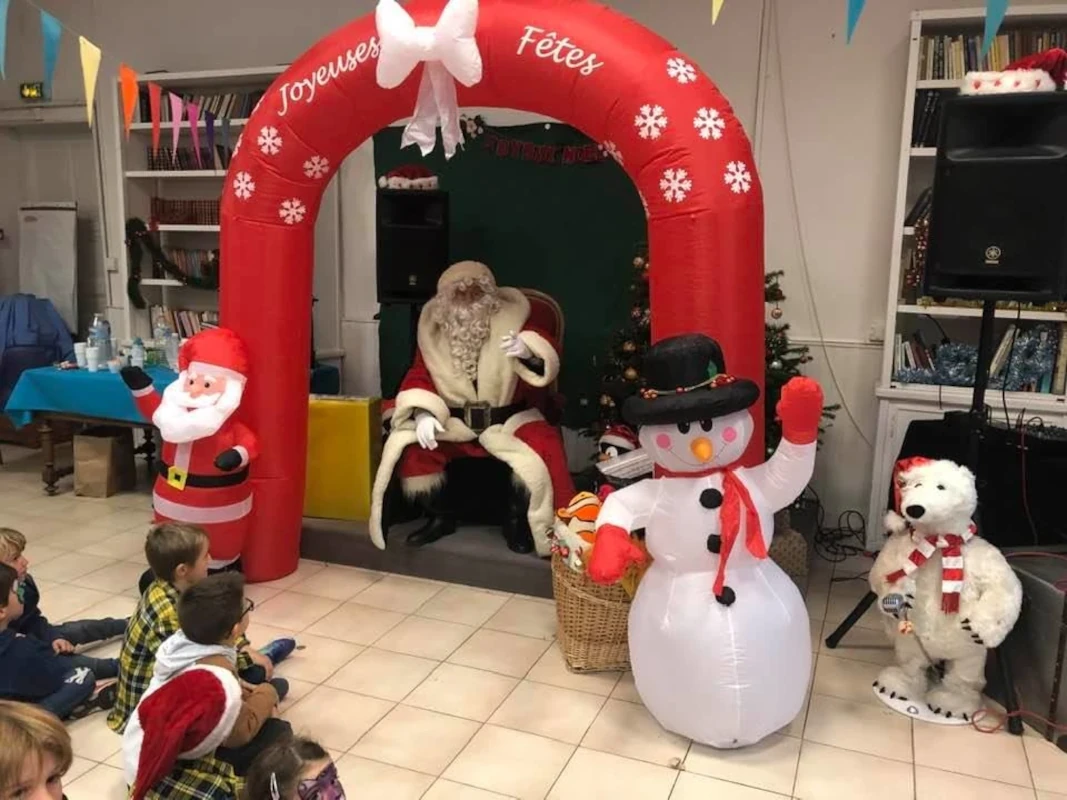 Père Noël sous une arche gonflable « Joyeuses Fêtes », entouré d'enfants