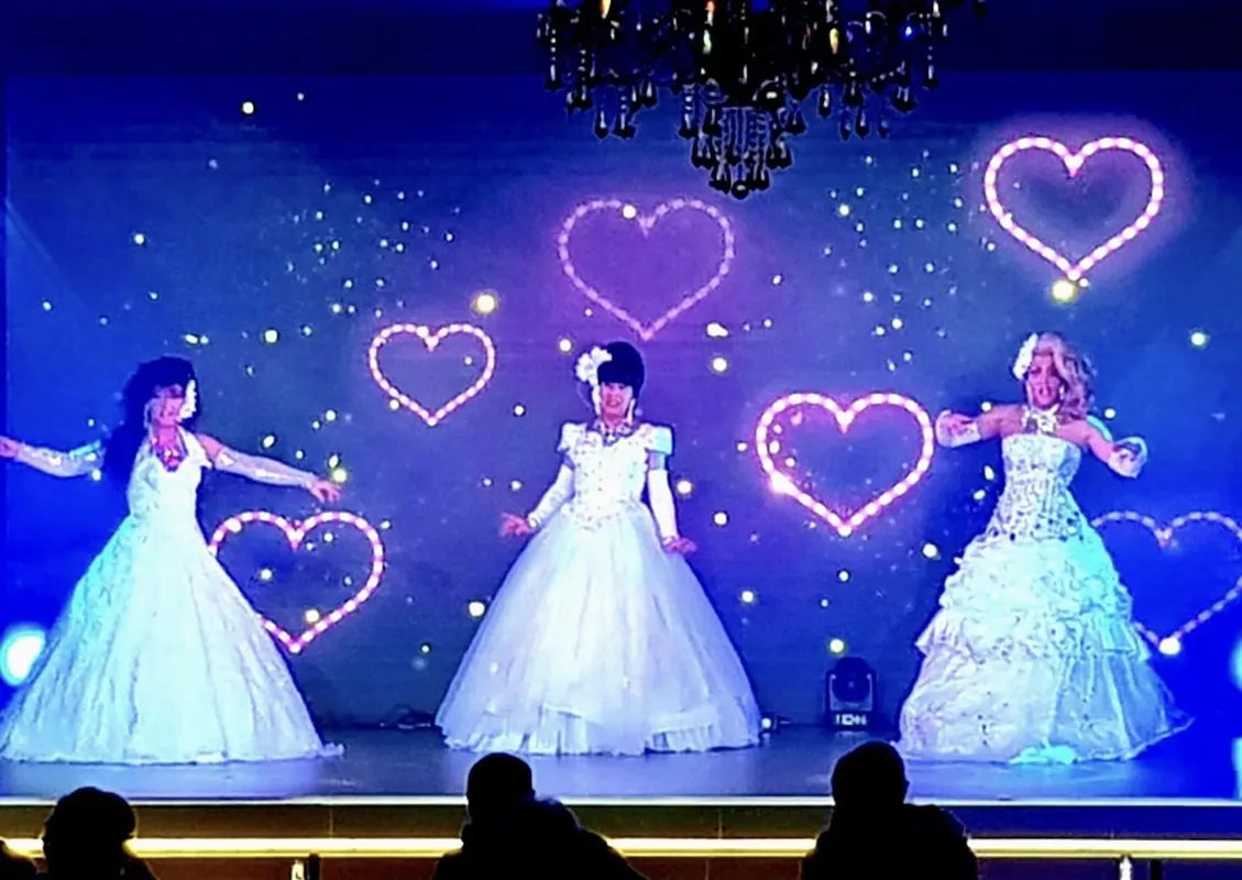Trio de transformistes en robes blanches, décor de cœurs lumineux