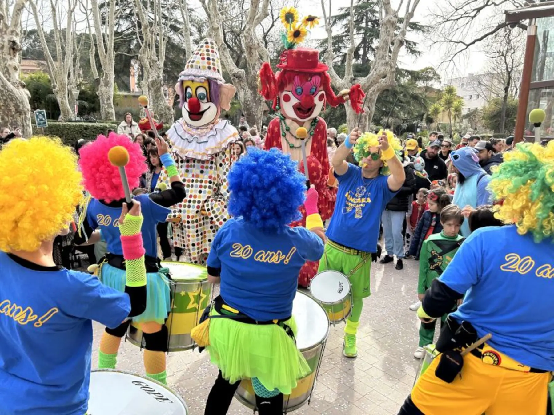 Géants et batucada en parade dans un parc, animation de rue