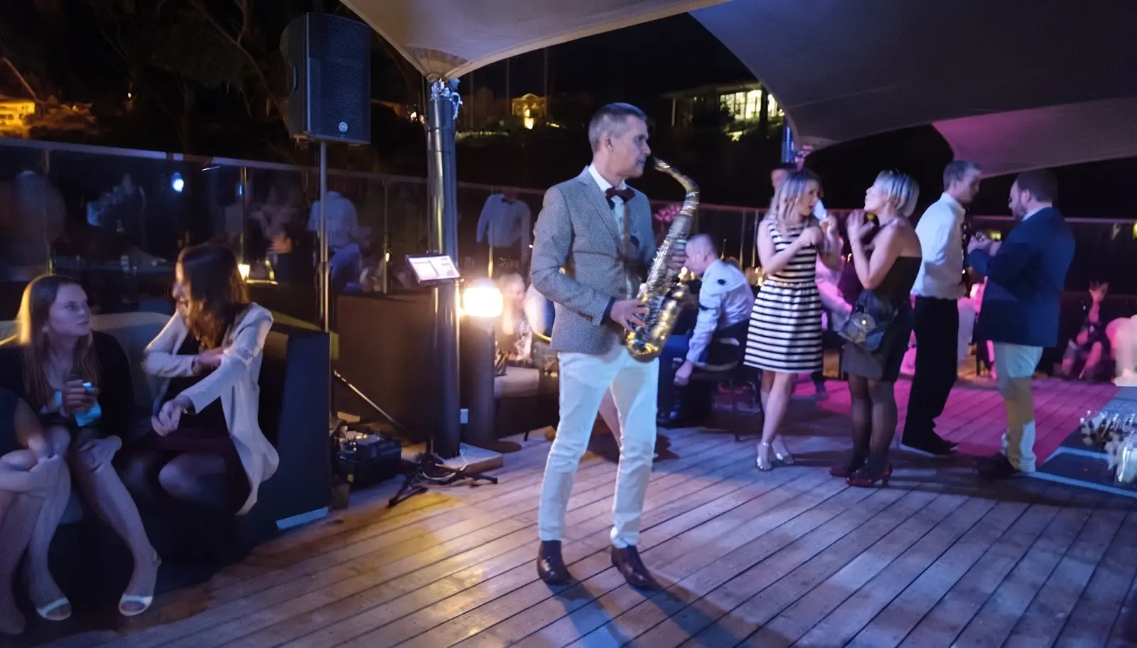 Saxophoniste en soirée sur une terrasse, entouré d'invités